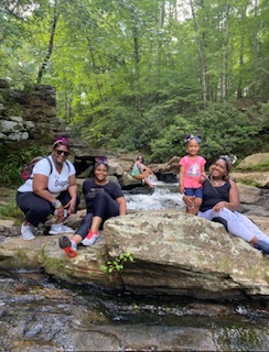 Village members resting on rocks beside a creek during a hike